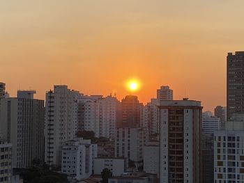 Buildings in city against romantic sky at sunset