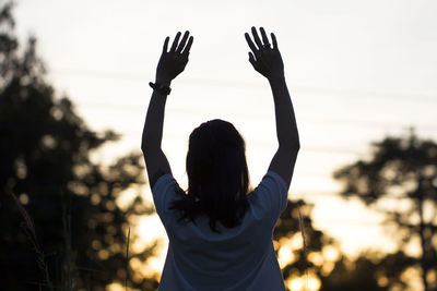 Rear view of woman with arms raised standing against clear sky