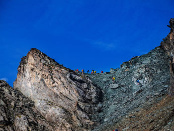 Low angle view of people on rock formation against blue sky