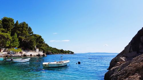 Boats moored in sea against clear blue sky