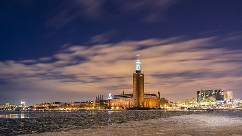 Illuminated buildings by river against sky at night