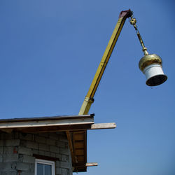 Low angle view of crane by building against clear blue sky