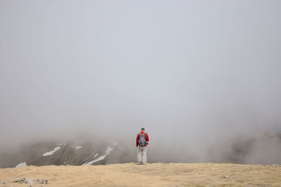 Rear view of man walking on landscape against sky