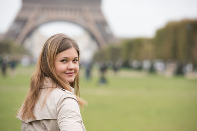 Portrait of smiling young woman standing against eiffel tower