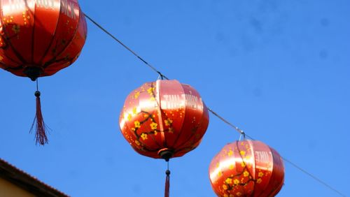 Low angle view of illuminated lanterns against clear blue sky