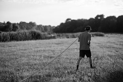 Rear view of young man holding rope while standing on grassy field at park during sunset