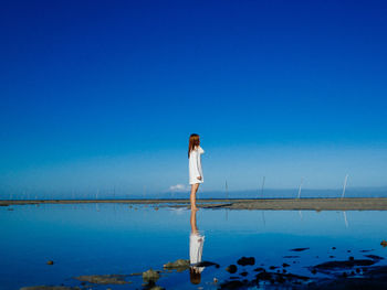 Woman standing by sea against clear blue sky