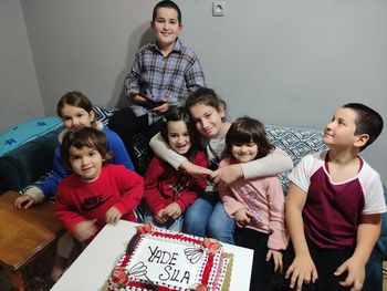 Portrait of cute kids sitting by birthday cake at home