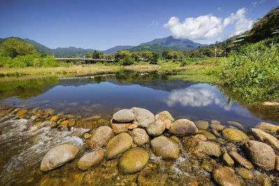 View of pond with rocks against trees and mountains in background