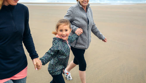 Playful woman walking with mother and daughter at beach