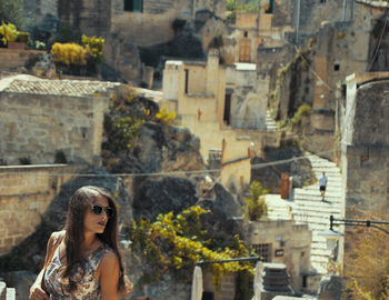 Young woman looking away while standing against building in city