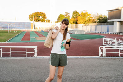 Teenager girl walking at the stadium with the papper bag after workout