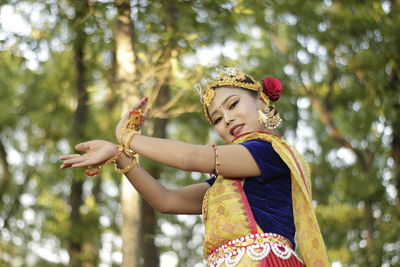 Midsection of woman with arms raised standing against plants