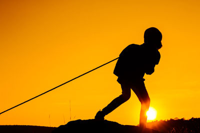 Silhouette girl pulling rope while standing on field against clear sky during sunset