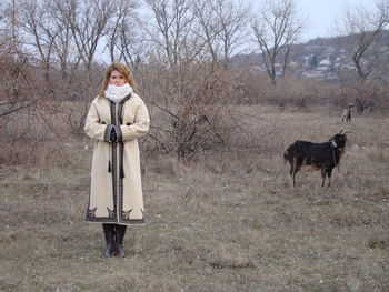 Portrait of woman standing against bare trees on field during winter