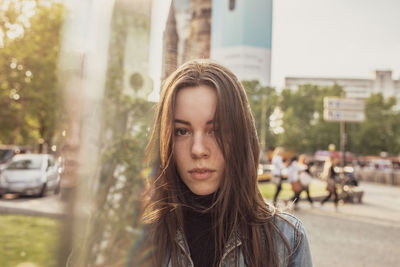 Portrait of beautiful young woman standing by glass in city