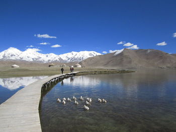 Scenic view of lake by mountains against blue sky