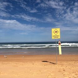 Warning sign on beach against sky