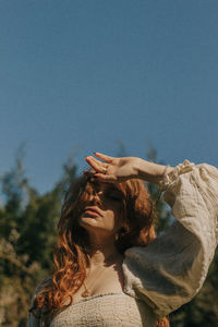 Low angle view of woman looking away against clear blue sky