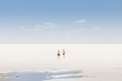 Friends walking on sand at beach against sky