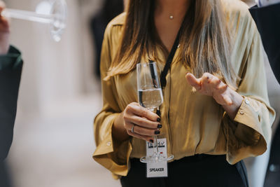 Midsection of businesswoman holding champagne flute while gesturing during seminar