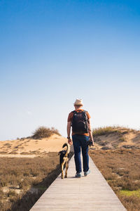 Rear view of woman walking with dog on umbrella against sky