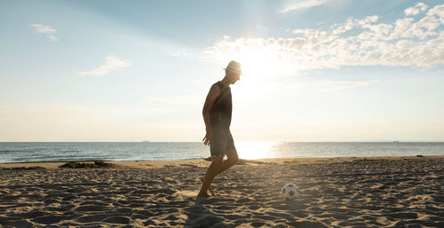 Man playing with soccer ball at beach against sky