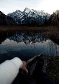 Low section of person sitting by lake against snowcapped mountain during sunset