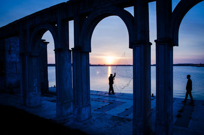 People fishing by river seen through arch during sunset