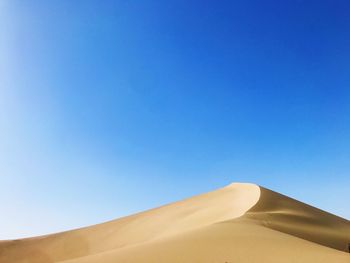 Low angle view of desert against clear blue sky