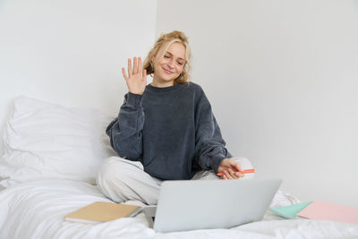 Young woman using laptop while sitting on bed at home