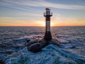 Lighthouse by sea against sky during sunset