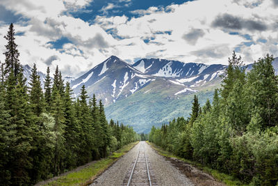 Railroad tracks leading towards mountains against sky