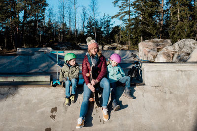 Mom sitting playing with her kids at a skatepark outdoors having fun