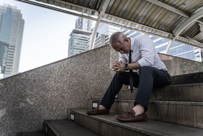 Low angle view of man sitting on glass wall