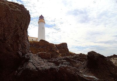 Low angle view of lighthouse by buildings against sky