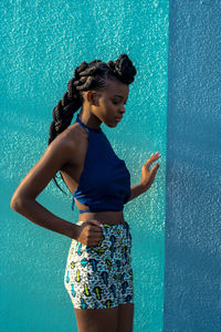 Young woman looking away while standing against blue wall