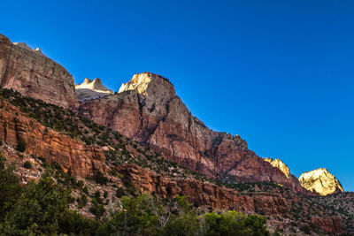 Low angle view of rocky mountains against clear blue sky