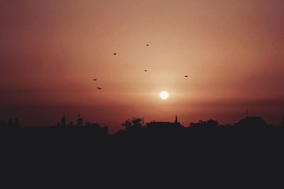 Silhouette birds flying against sky during sunset