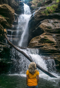 Rear view of man surfing in waterfall