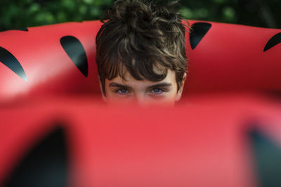 Boy peers out from hole in watermelon float on summer beach vacation