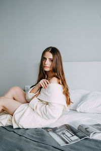 Portrait of young woman sitting on bed at home