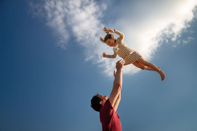 Low angle view of father throwing daughter against sky