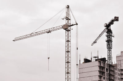 Low angle view of cranes at construction site against sky