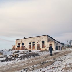 Rear view of woman walking by building against sky during winter