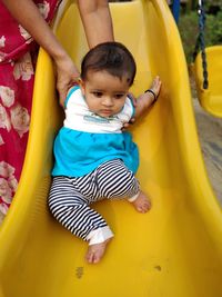 Midsection of mother with toddler daughter on slide at playground