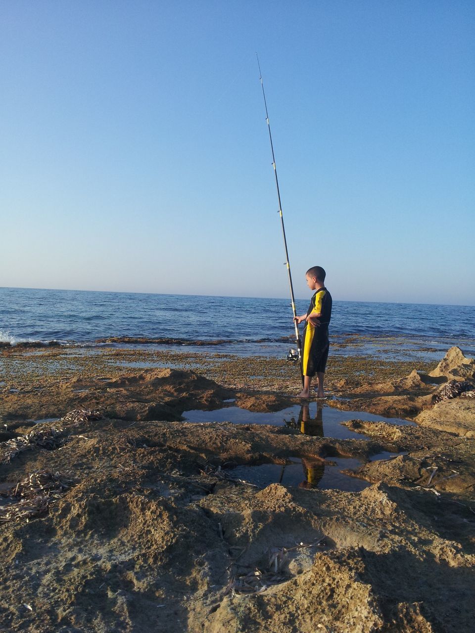 water, sea, full length, lifestyles, leisure activity, casual clothing, horizon over water, clear sky, standing, beach, rear view, copy space, sky, vacations, shore, nature, scenics, beauty in nature