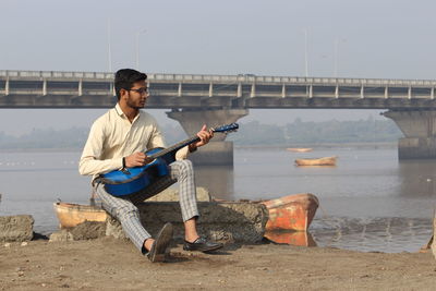 Full length of man sitting on bridge against sky