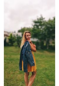 Portrait of smiling young woman holding denim jacket while standing on field