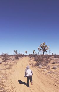Rear view of woman walking on desert against clear blue sky